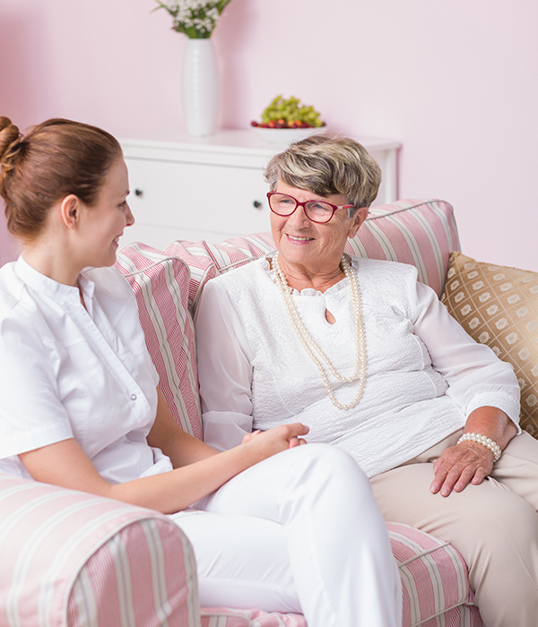 Caregiver and elderly woman smiling and talking while seated together on a couch